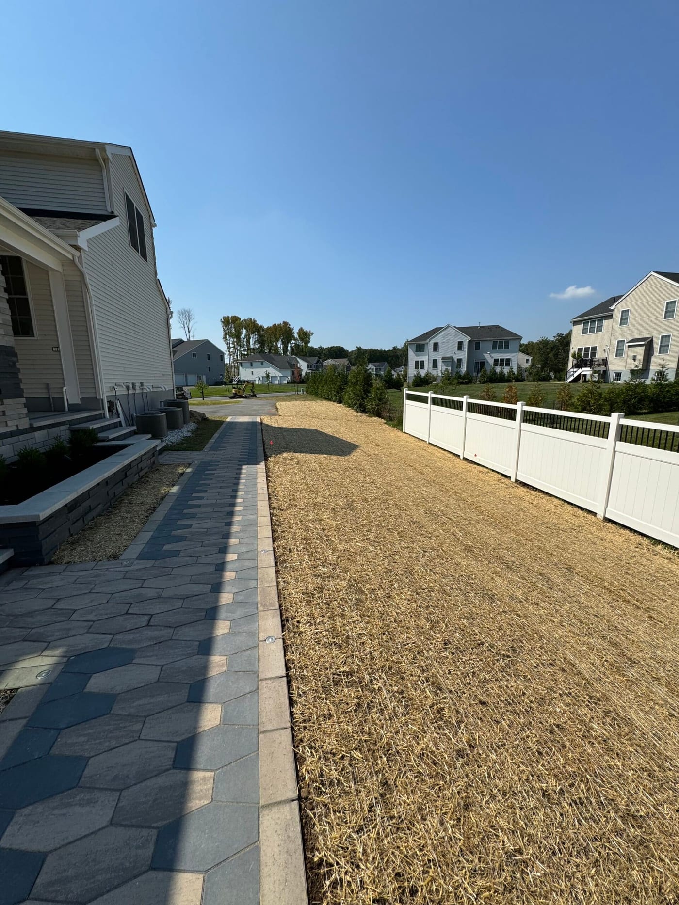 Freshly graded and seeded yard sloping away from a home beside a paver walkway