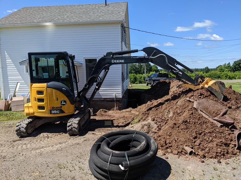Nomad excavator beside a home with drain tile staged for an exterior drainage install